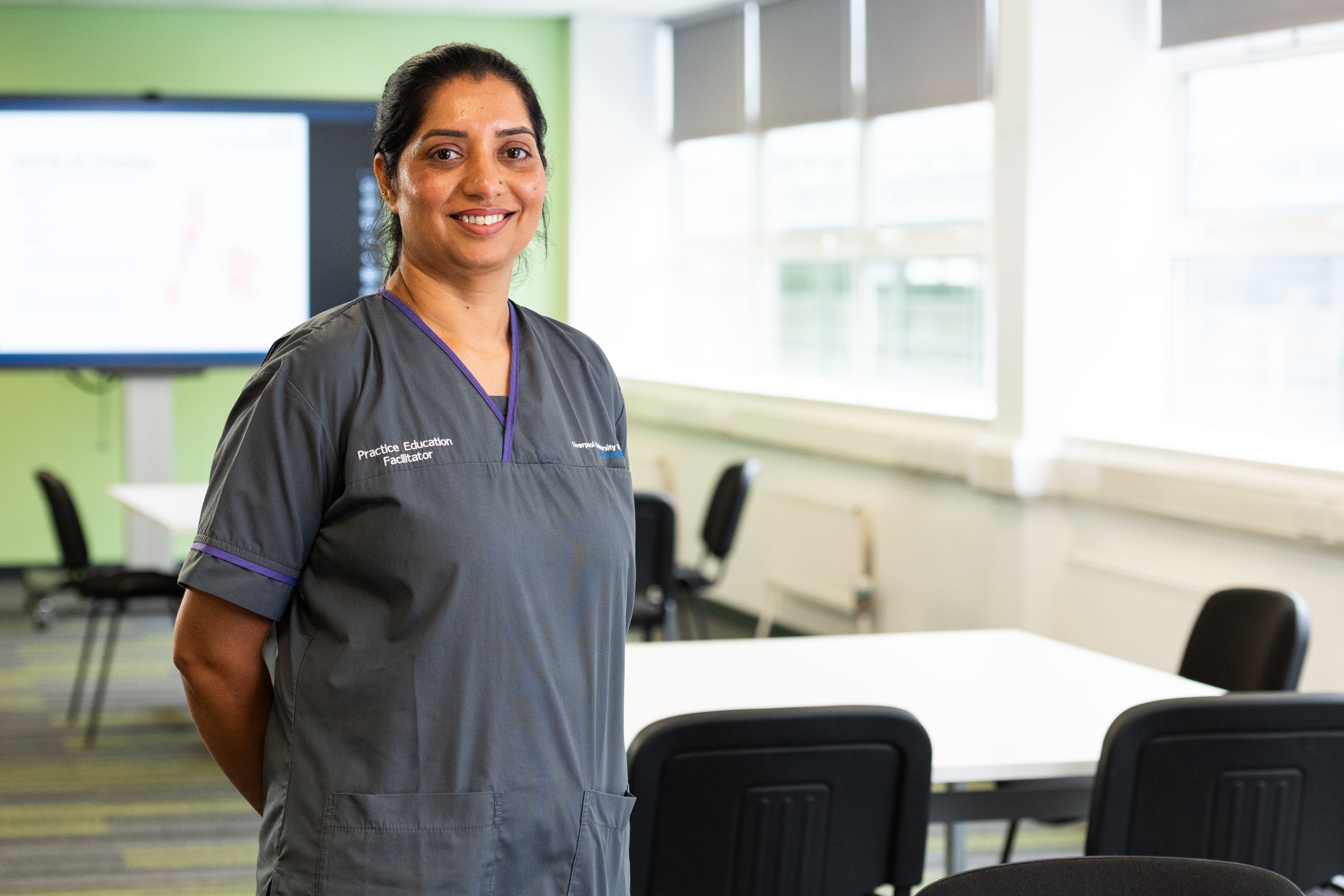 Kulwinder Kaur has a big smile on her face after being recognised by the RCN. Kulwinder is in her Practice Educator uniform, which is grey with a purple collar. She is stood in Aintree's Learning and Development Suite where she helps develop future NHS colleagues reach their full potential.