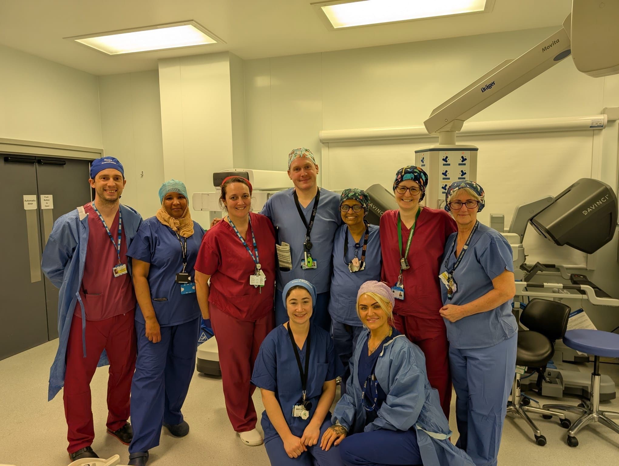 Nine members of the robotic surgery team standing in theatre, smiling to camera